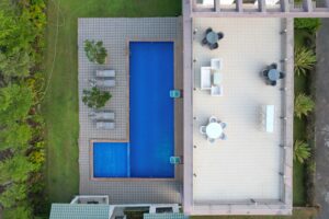 A construction crew installing an inground pool shell in a residential backyard with landscaping and machinery visible.
