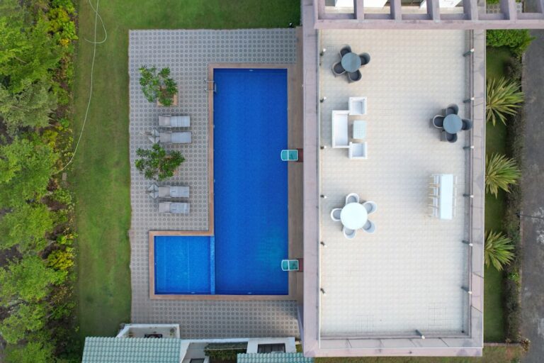 A construction crew installing an inground pool shell in a residential backyard with landscaping and machinery visible.