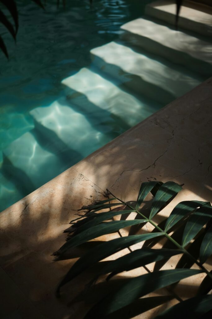 Lush landscaping surrounds a backyard pool with non-slip stone paving and neatly trimmed shrubs.