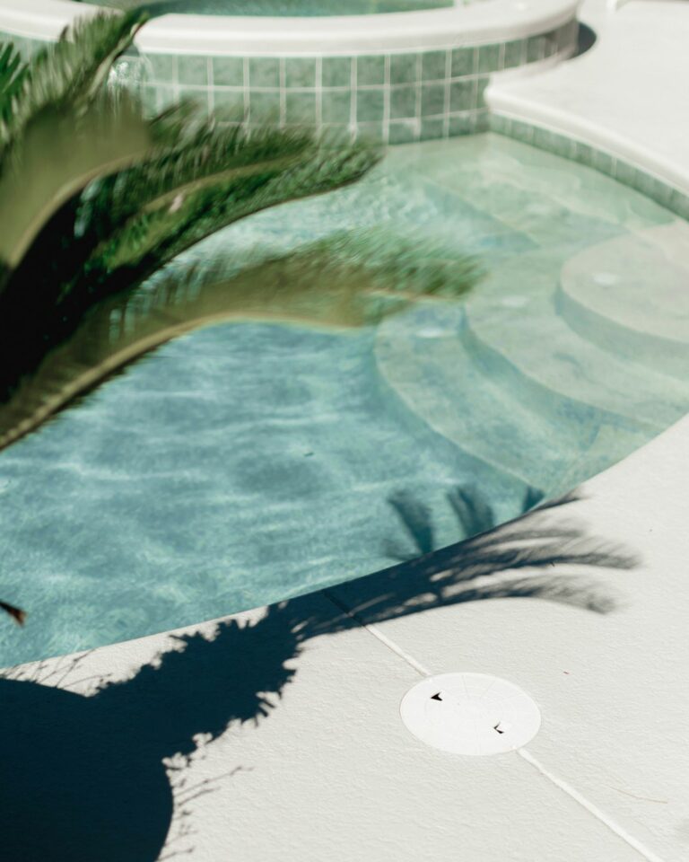 A backyard pool with a person brushing the wall and using a skimmer to collect leaves.