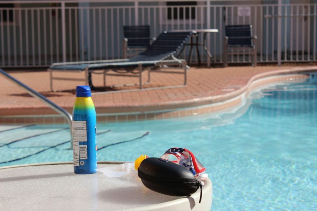Homeowner testing pool water beside a skimmer net, brush, vacuum head, and chemical measuring tools.